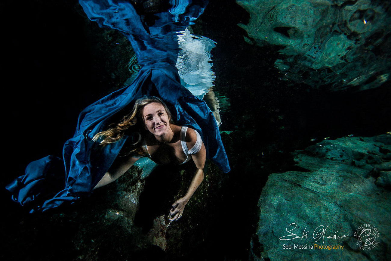 Bride playing with a blue fabric during an underwater trash the dress in a Mexican cenote.