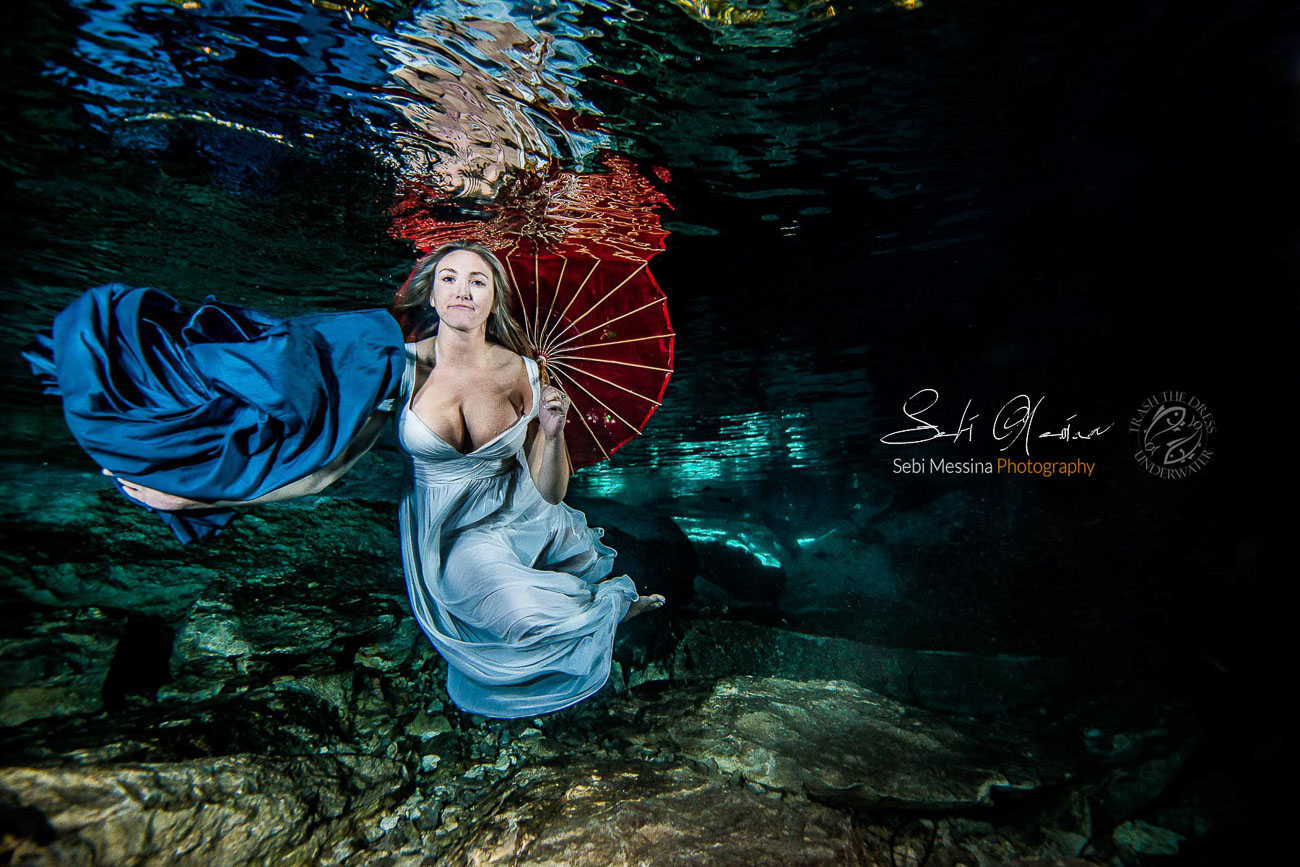 Bride with umbrella and a blue fabric, while modelling underwater in a cenote in Mexico - Sebi Messina Photography