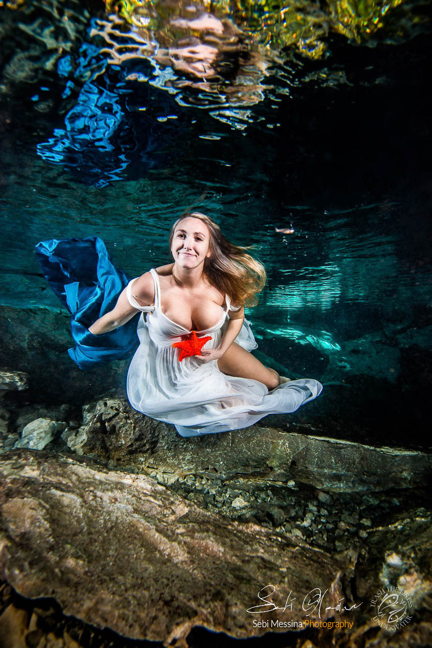 Bride with a starfish and a blue fabric, while modelling underwater in a cenote in Mexico - Sebi Messina Photography