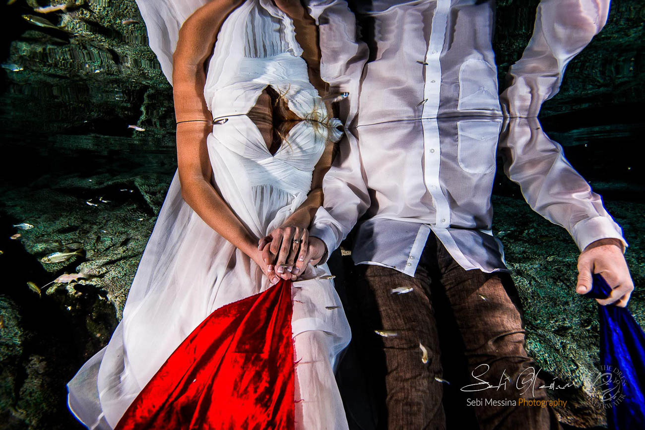 Bride and groom hand in hand underwater in a cenote